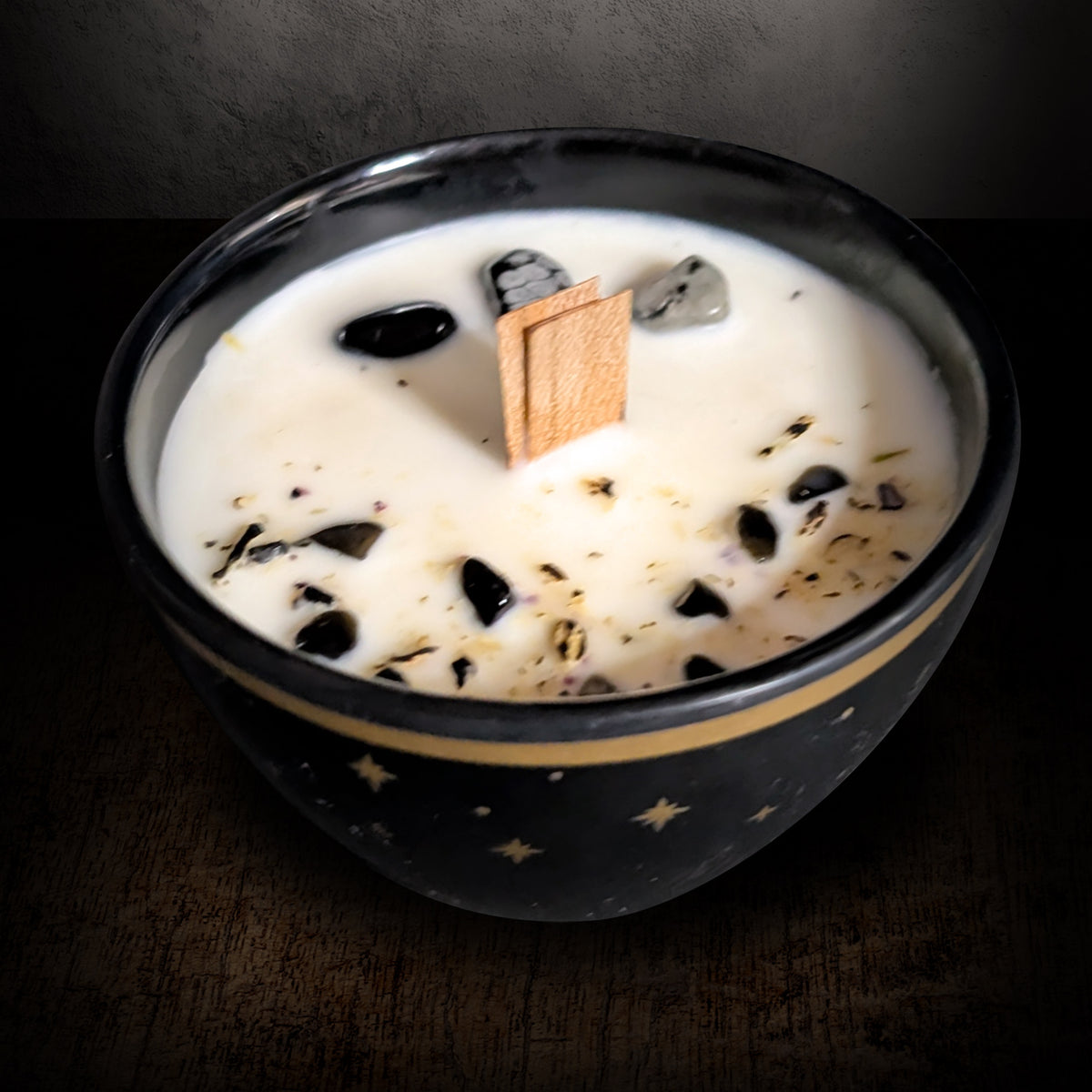 Black star candle seen from above on a dark background, showing the black and snowflake obsidian pieces set into the wax surface beside the wooden wick