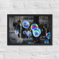 Bubbles of Barcelona framed luster print by iain, black framed photograph of large rainbow colored soap bubbles floating in front of a nearly black and white city square, hanging on a white brick wall