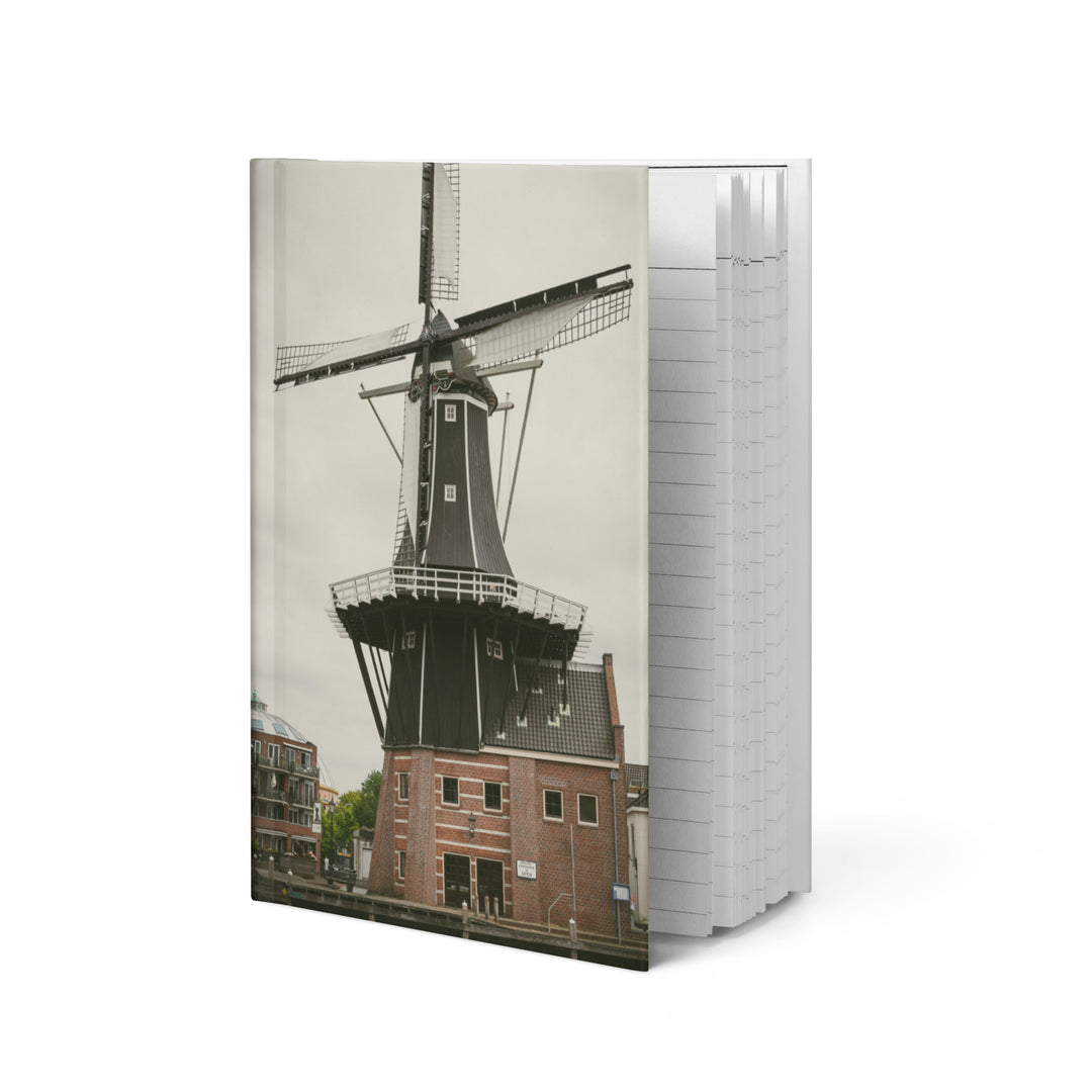 De Adriaan Windmill hardcover journal by iain, journal standing upright on a white background, with a photograph of the De Adriaan windmill in Haarlem and its brick building on the front cover and the page edges showing on the side