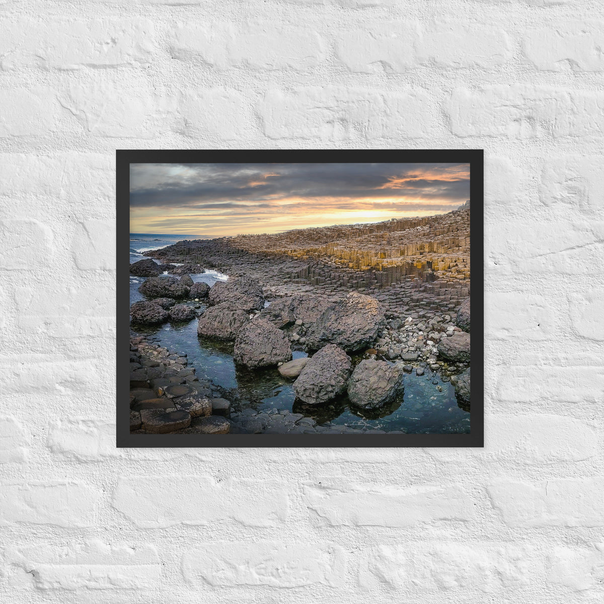 Giant's Causeway, Northern Ireland framed luster print by iain, larger black framed print hanging on a white brick wall