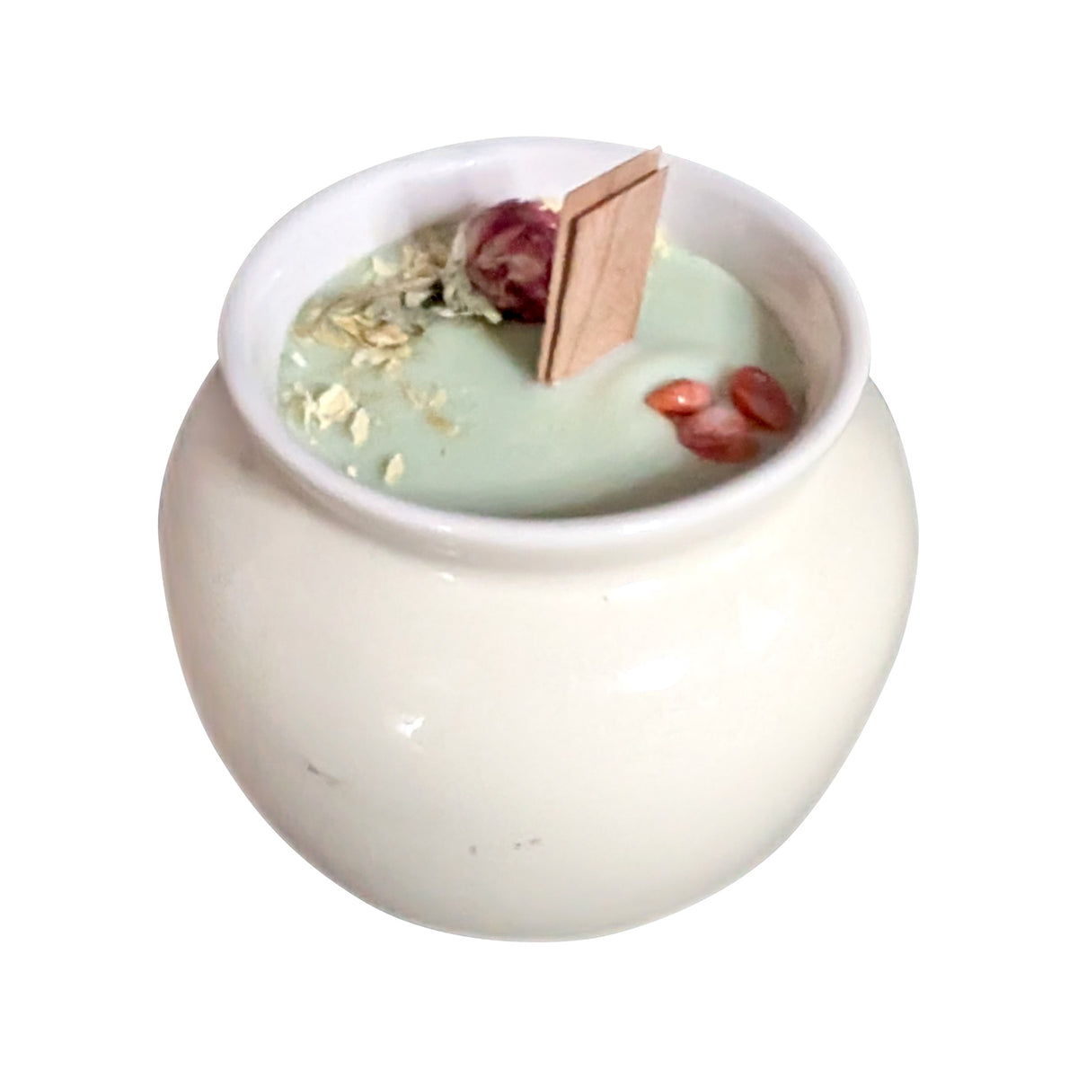 Cream porcelain pot candle seen from a high angle on a white background, showing the pale green wax surface set with dried flowers and red agate