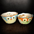 Pair of owl shaped ceramic candles standing side by side on a dark background, soy wax poured level with the rim and topped with dried chrysanthemum petals and small stones