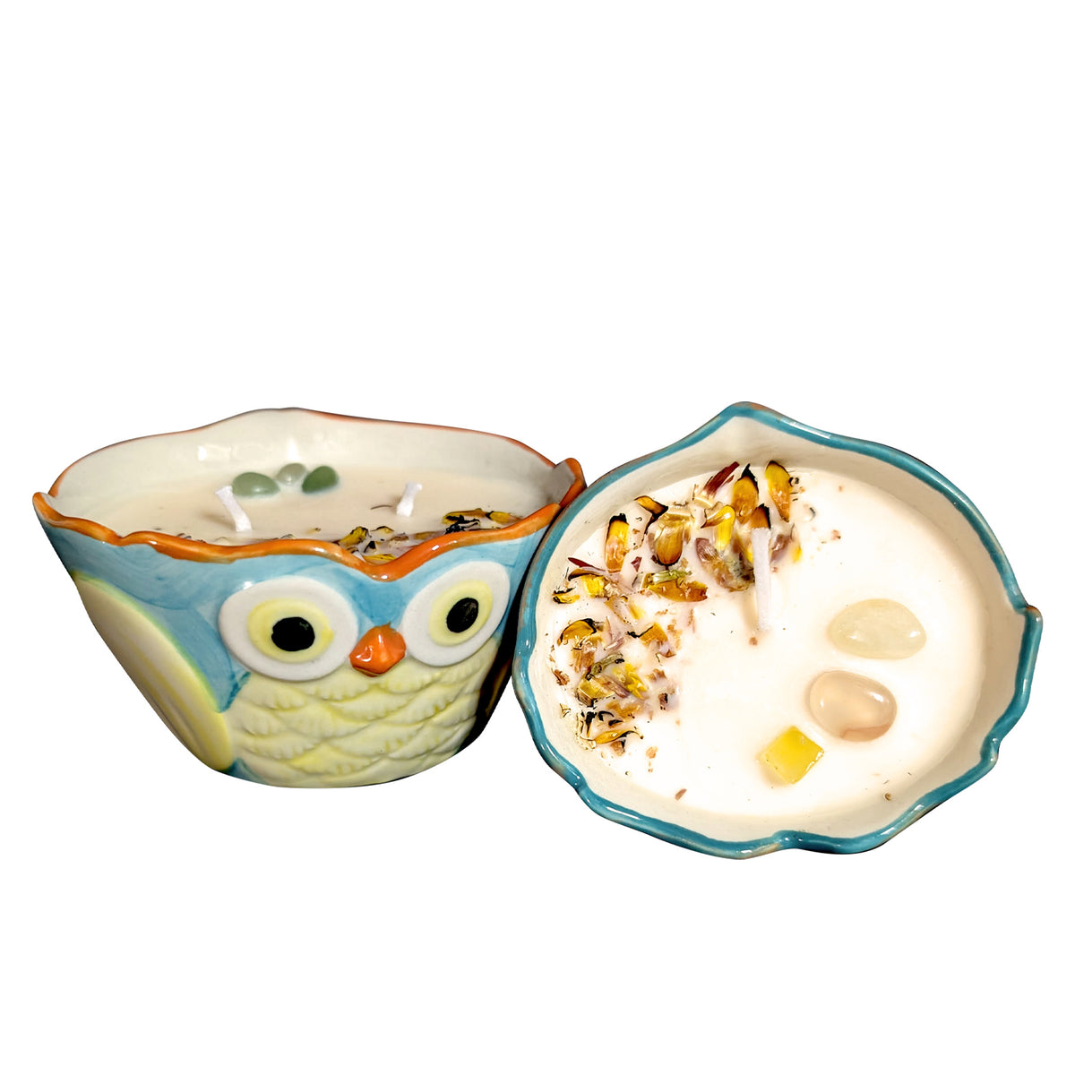 Pair of owl shaped ceramic candles on a white background, one standing upright and one tipped onto its side to show the wax surface with dried petals and stones