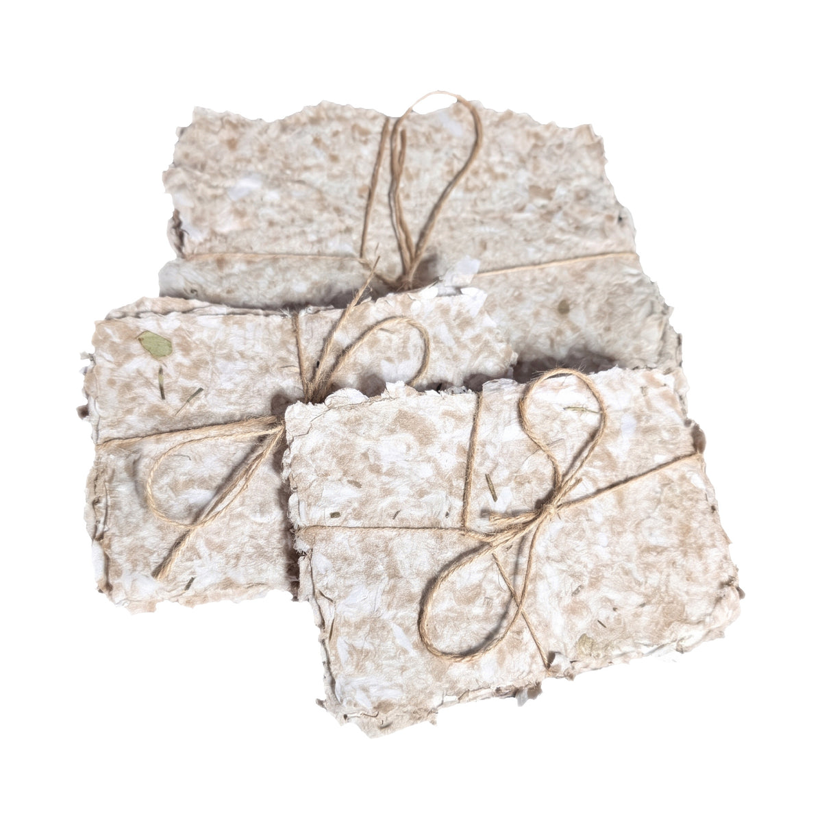 Bundles of handmade paper tied with twine, shown close up from the front on a white background, rough deckle edges and herb flecks visible in the pulp