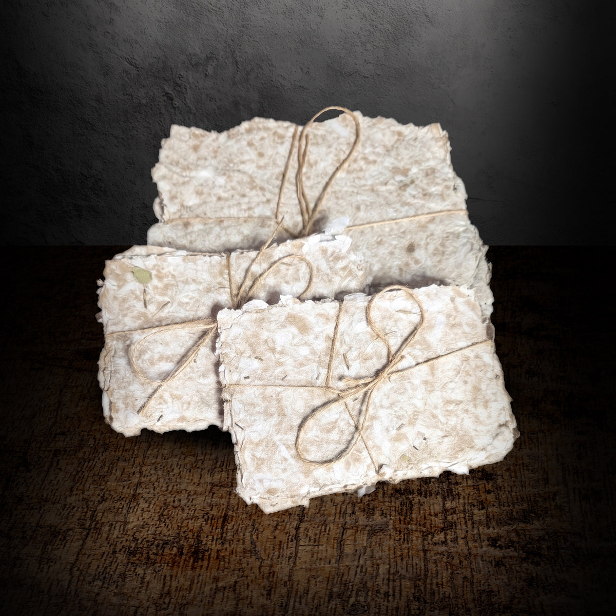 Three bundles of handmade paper tied with twine arranged together on a dark background, showing both the small and large sheet sizes