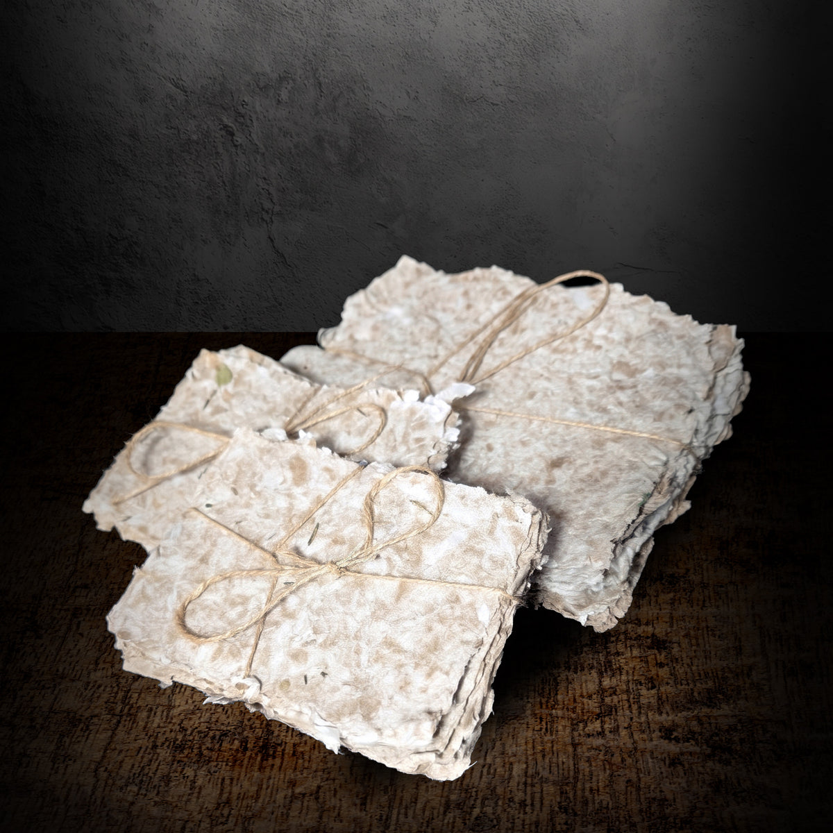 Bundles of handmade paper tied with twine seen from the side on a dark background, showing the stacked sheet thickness and uneven edges
