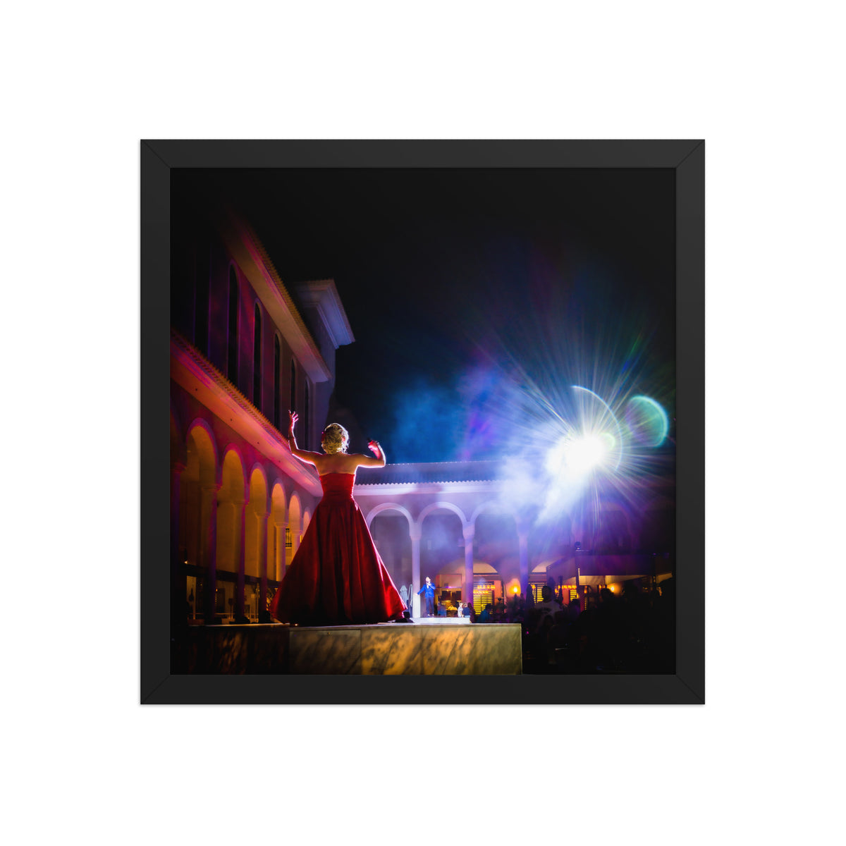Perform for the Gods framed luster print by iain, front view of a square black framed photograph of a performer in a red gown raising her arms toward the night sky, with smoke, arches, and a burst of stage light in a Tenerife courtyard