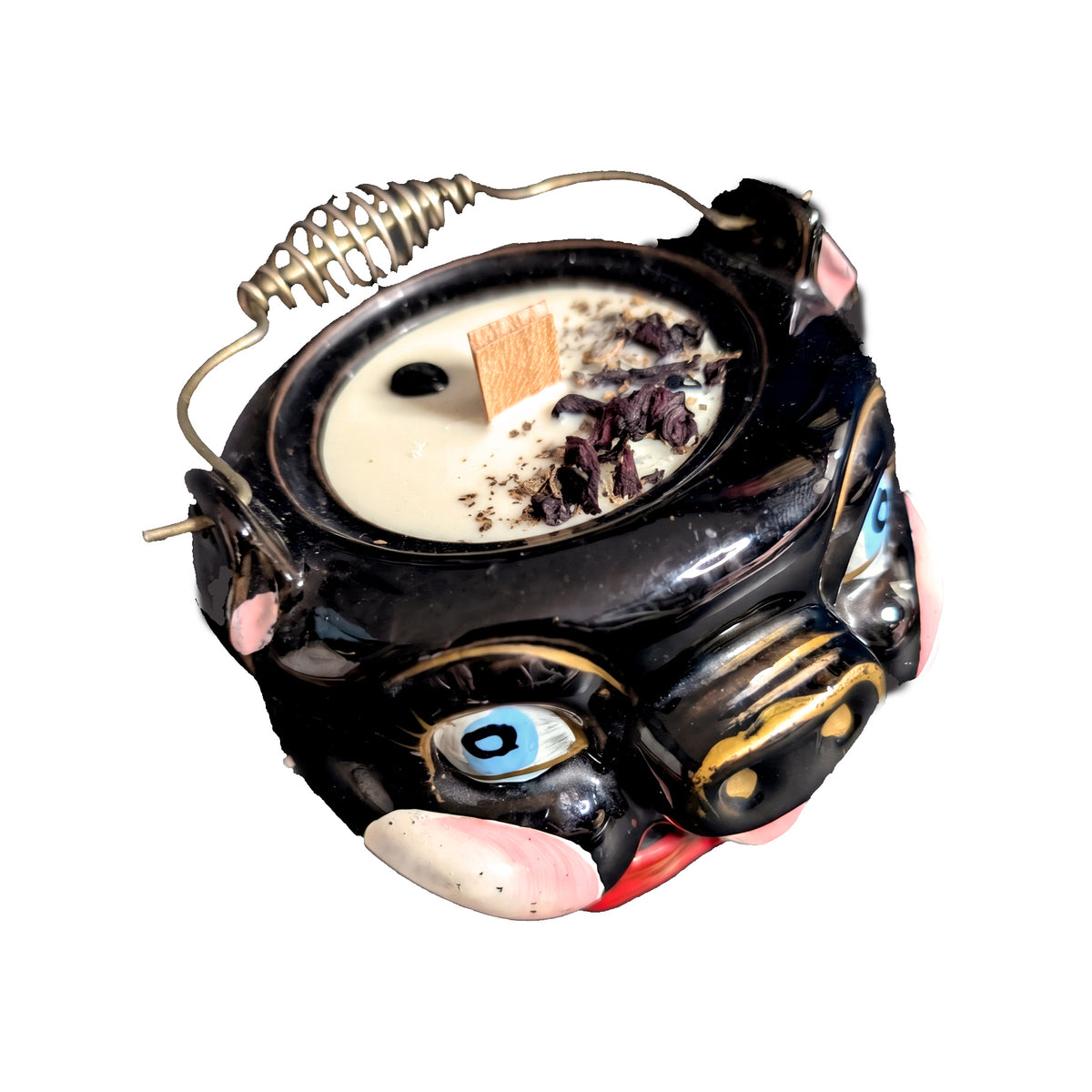 Black ceramic pig candle seen from a high angle on a white background, showing the wax surface set with obsidian chips and dried petals and the wire bail handle across the top