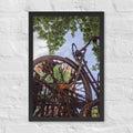 Rusty Bicycle framed luster print by iain, black framed photograph of a rusted bicycle overgrown with roots and moss under green leaves and blue sky, hanging on a white brick wall