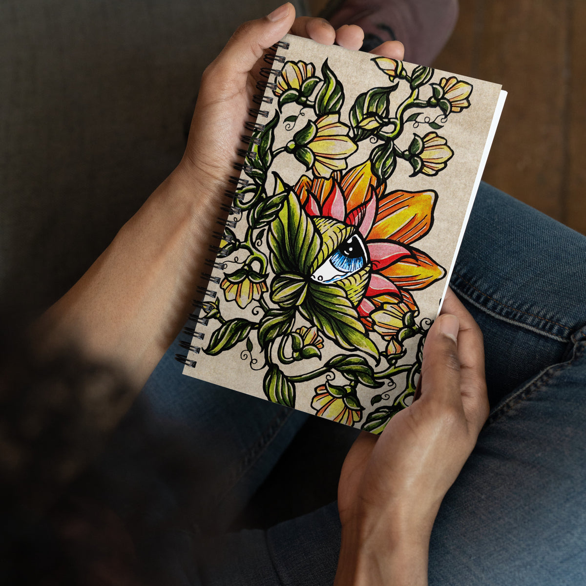 Person sitting in jeans holding the Watchful Nature spiral notebook open in both hands