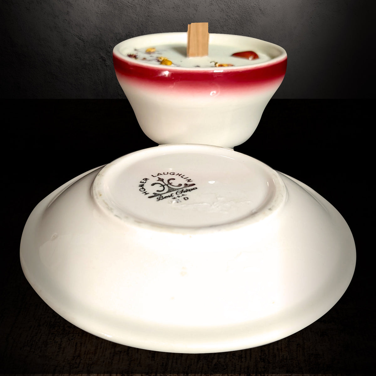 Saucer turned over in front of the red and white teacup candle on a dark background, showing the stamp on the underside