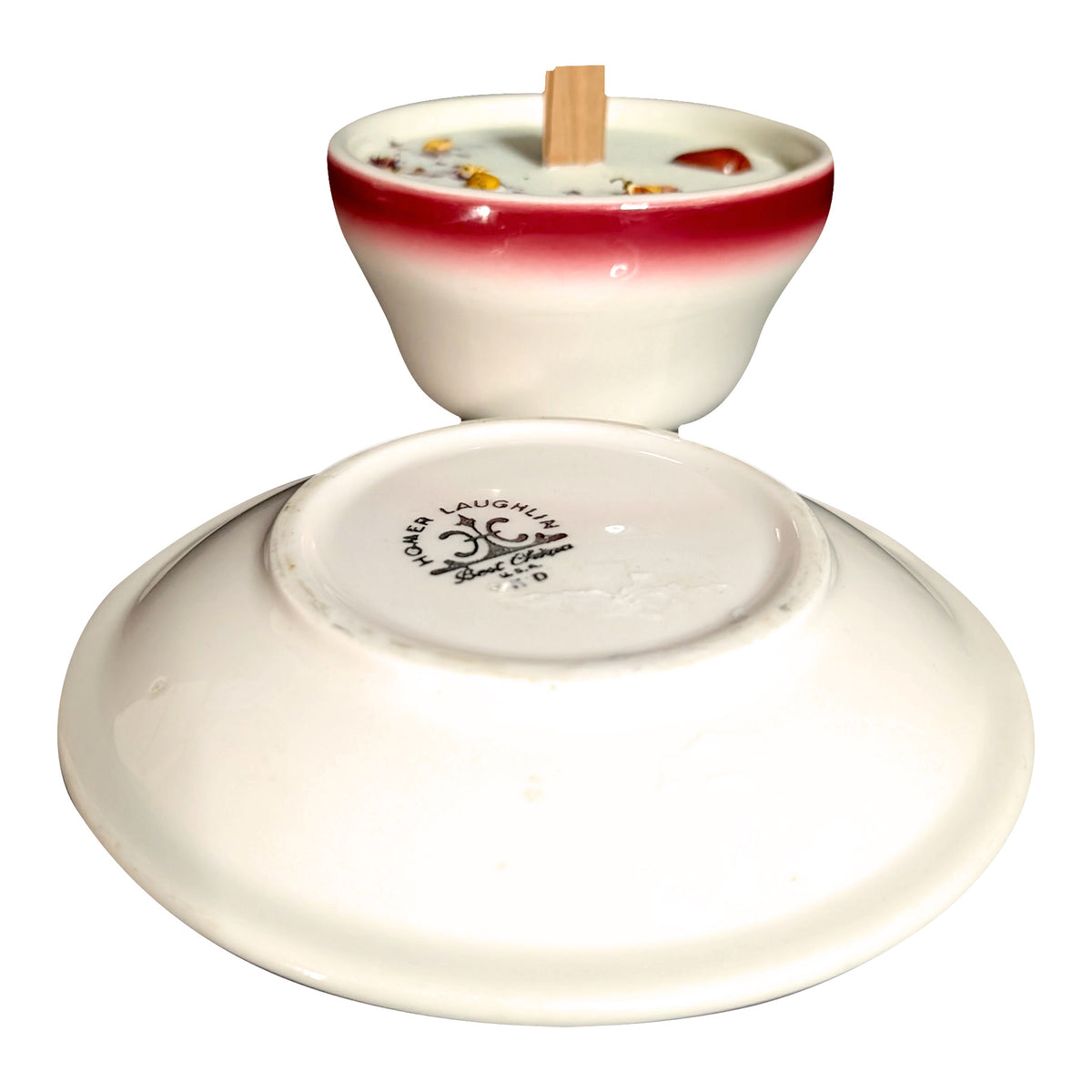 Saucer turned over in front of the red and white teacup candle on a white background, showing the stamp on the underside