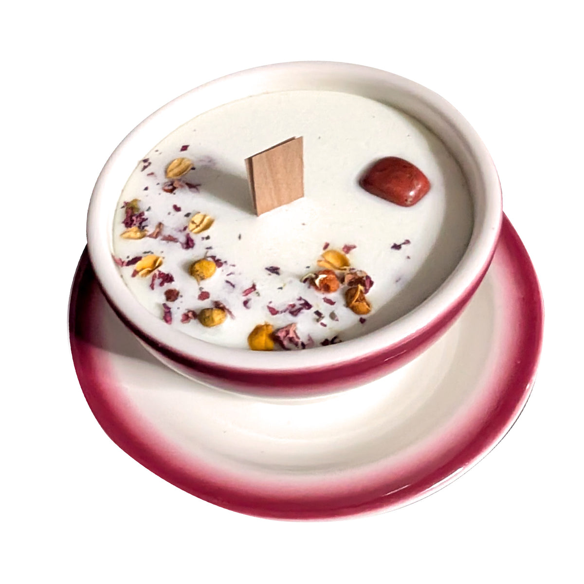 Red and white teacup candle seen from above on a white background, dried flower petals and botanicals pressed into the wax surface