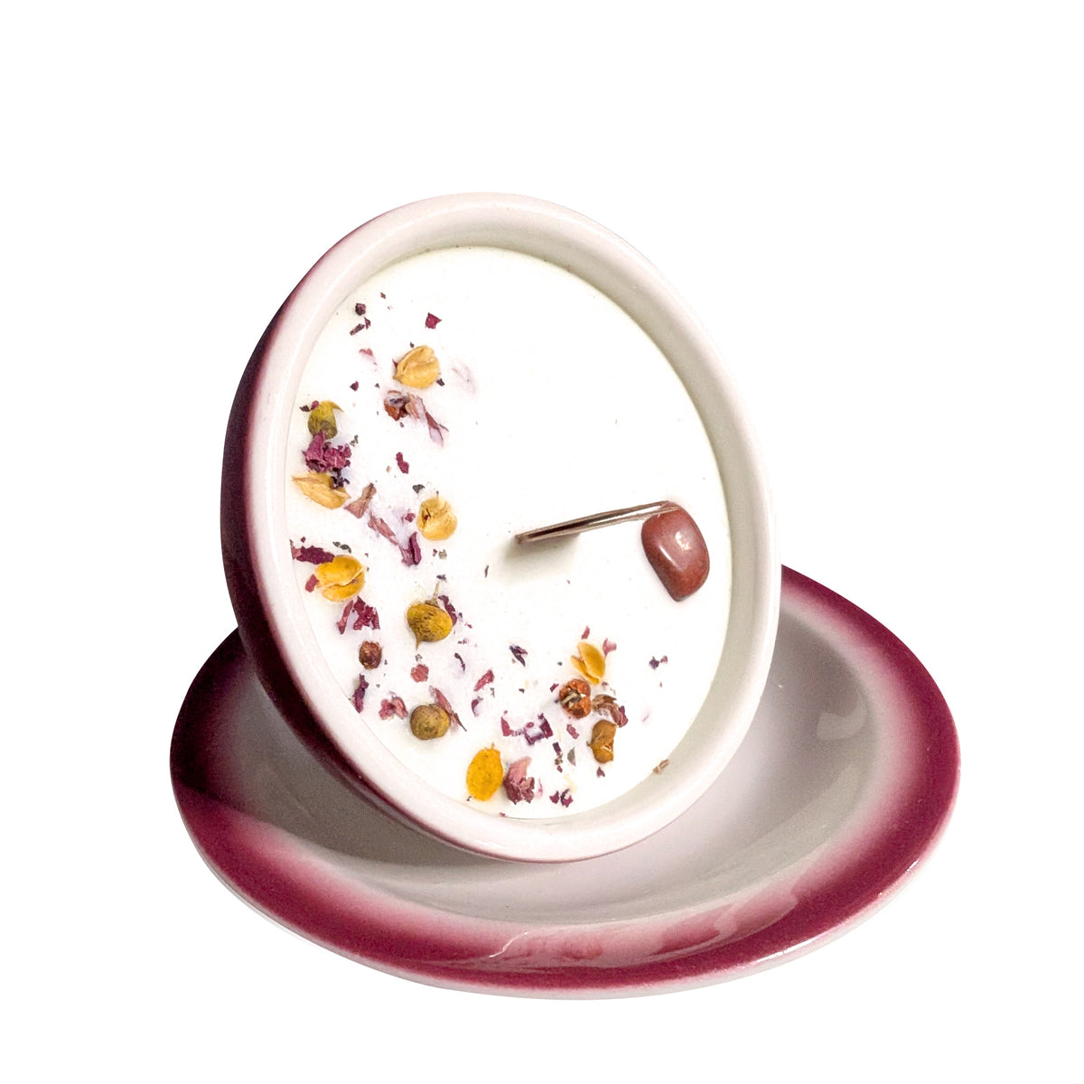Red and white teacup candle tipped forward on its saucer on a white background, showing the wax surface and wooden wick