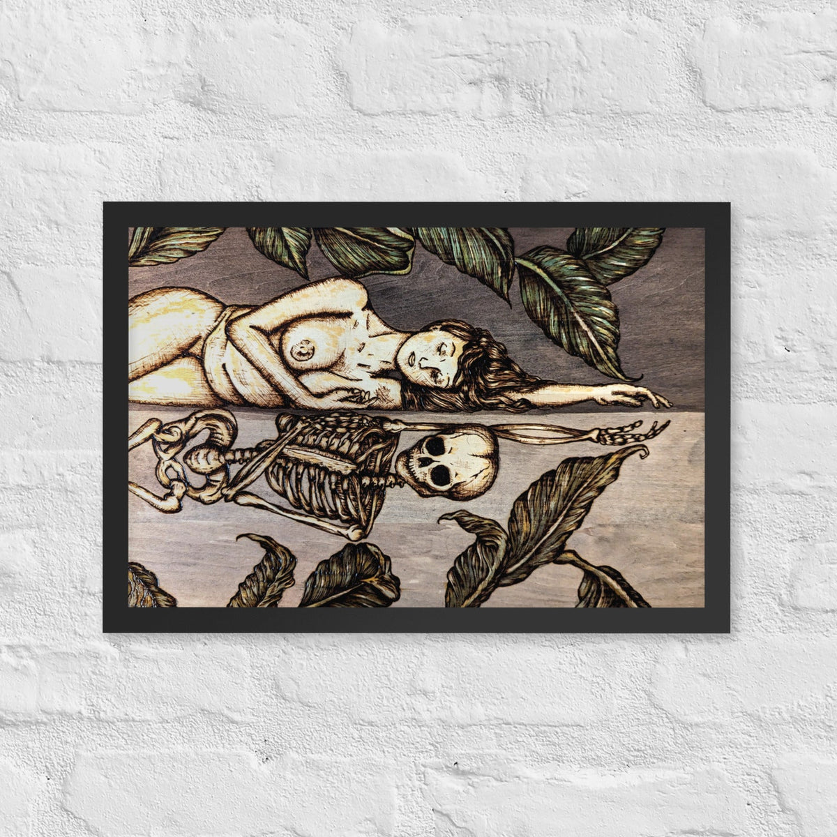 Vainglorious Contrition framed luster print by Cami Thunder, black framed print of a pyrography and watercolor piece on wood showing a reclining nude woman above a skeleton in the same pose, surrounded by dark leaves, hanging on a white brick wall