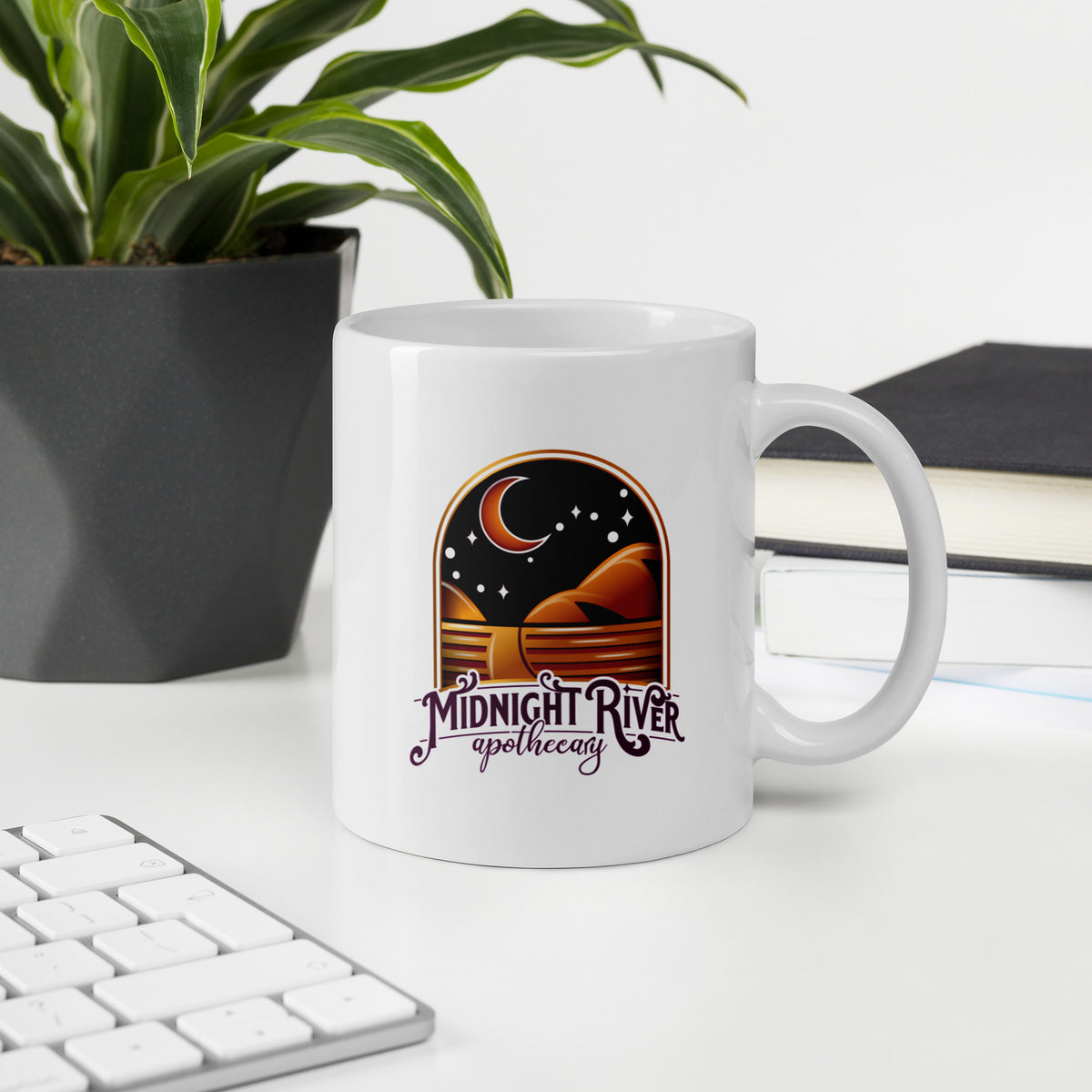Reclamation & Midnight River mug in white on a desk beside a keyboard and a potted plant, the Midnight River Apothecary badge facing the camera